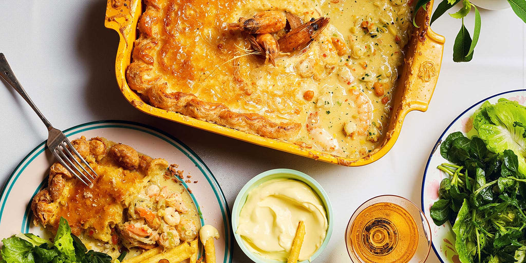 Prawn and crab pastry pie on a table with a salad, a pot of mayonnaise and a glass of wine