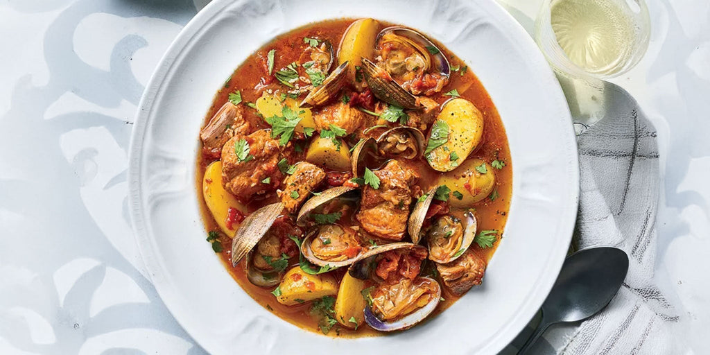 Pork and clam stew in a bowl on a table with a glass of wine.